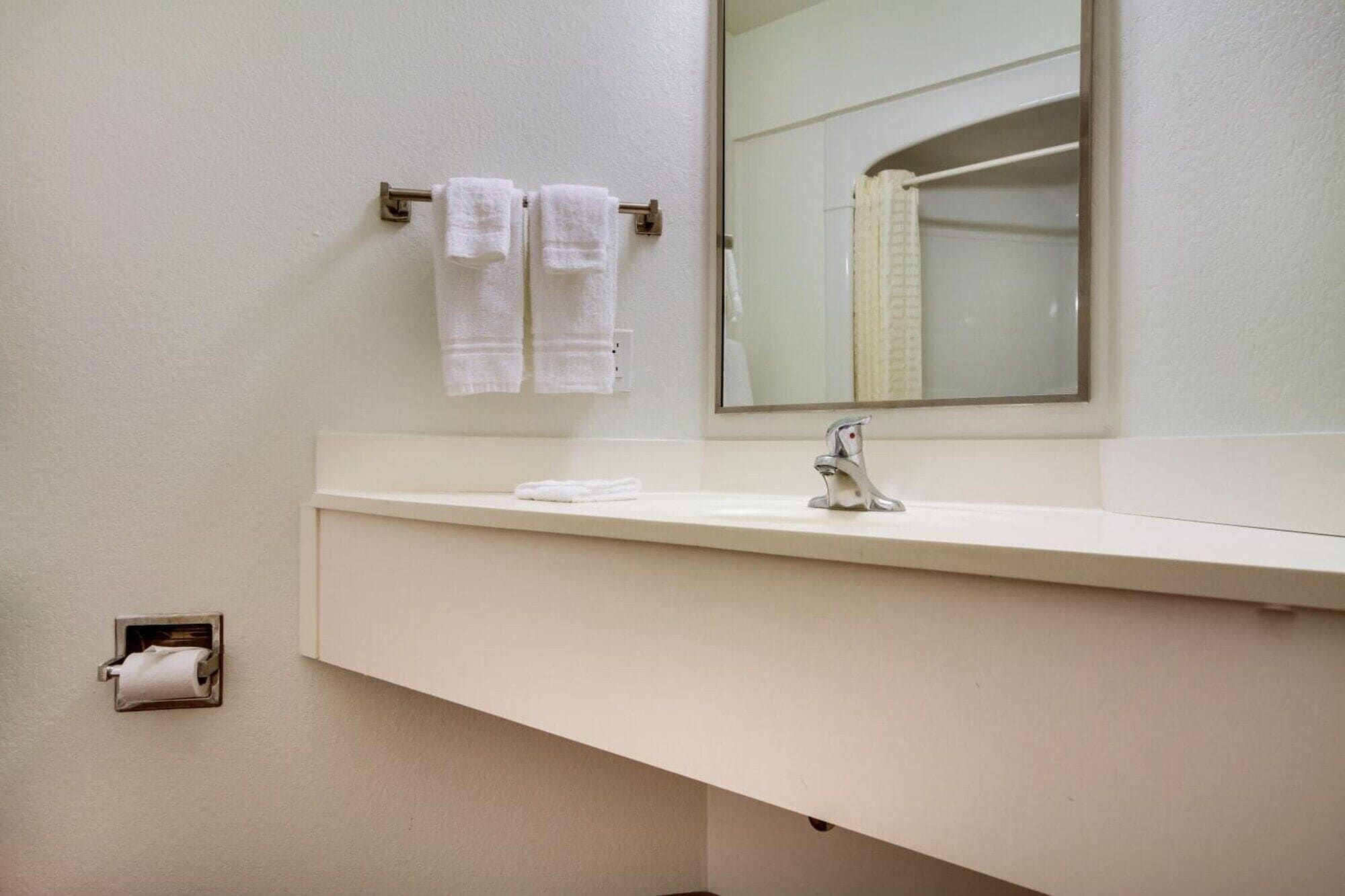 A bathroom with a white sink, a mirror, and two towels hanging on a towel rack.