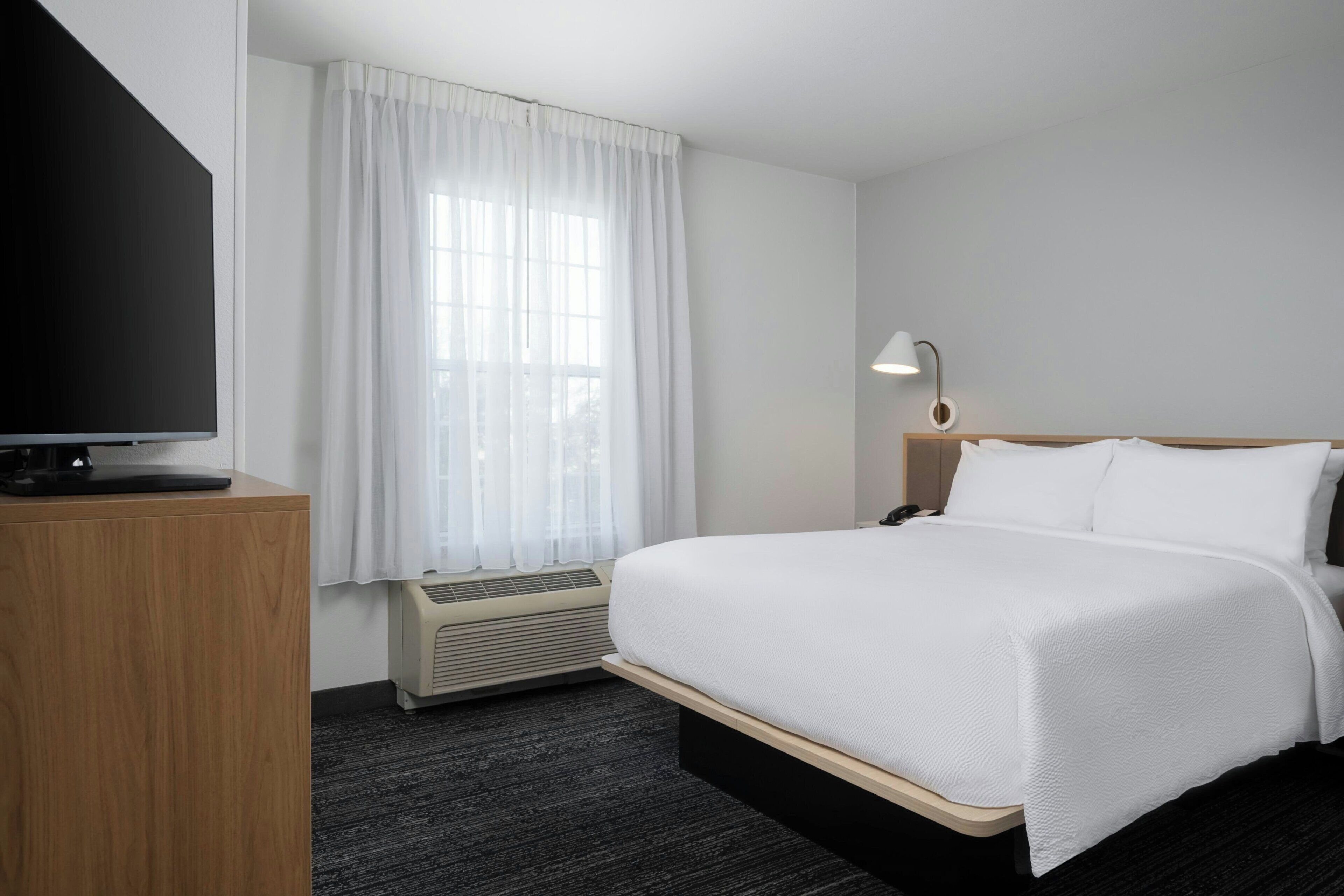 Hotelkamer met een bed, bureau met een flatscreen televisie, lamp en raam met gordijnen.