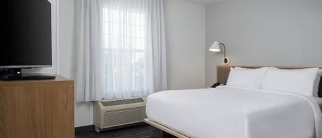 Hotelkamer met een bed, bureau met een flatscreen televisie, lamp en raam met gordijnen.