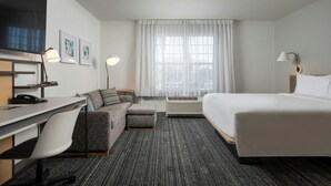 Una habitación de hotel con cama, escritorio con silla, sofá, televisor y ventana con cortinas.