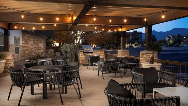 Un patio al aire libre con mobiliario de mimbre, pared de piedra y luces colgantes.