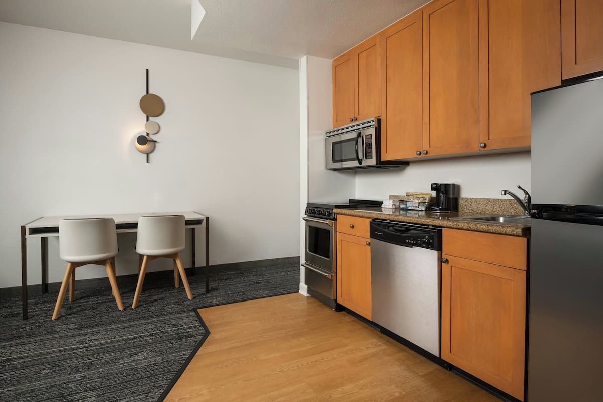 A modern kitchen with wooden cabinets, a microwave, a dishwasher, and a dining area with two chairs.