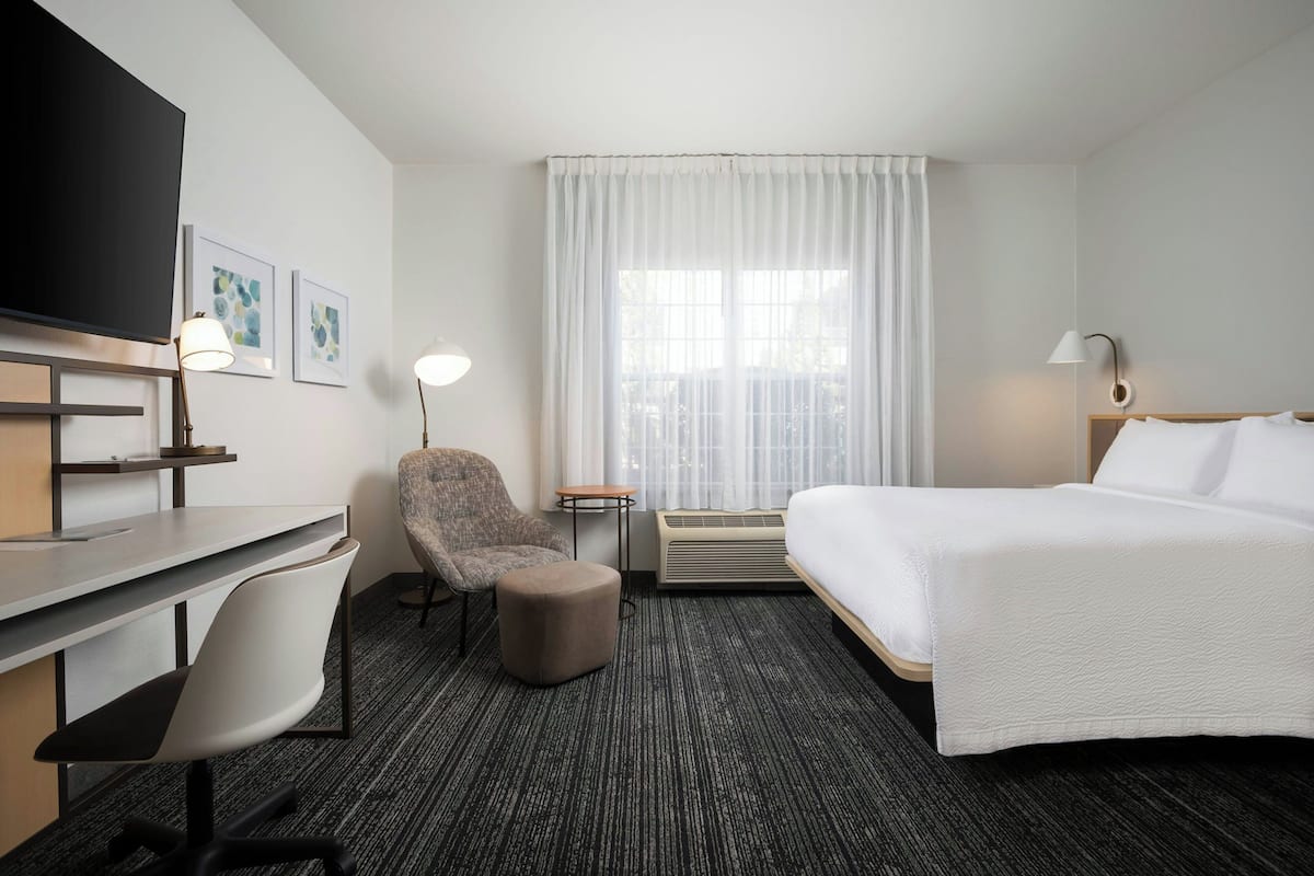 A hotel room with a bed, desk, chair, and a television.