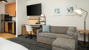Una habitación de hotel moderna con kitchenette, una televisión de pantalla plana, un escritorio, un sofá y una lámpara.