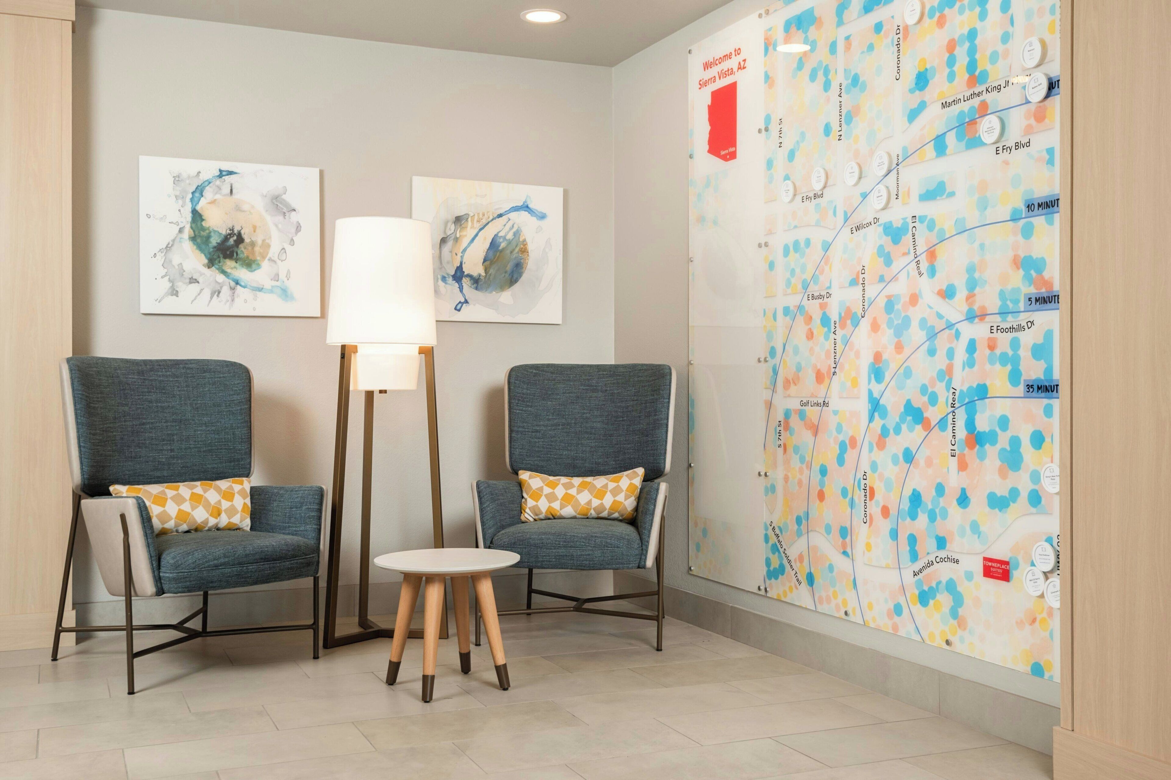 A lobby with two armchairs, a floor lamp, a small table, and a map on the wall.