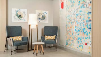 A lobby with two armchairs, a floor lamp, a small table, and a map on the wall.
