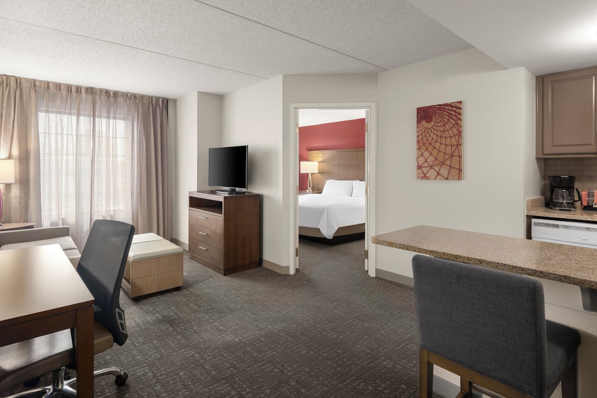 Habitación de hotel con escritorio, silla, televisor y cama con cabecera roja.