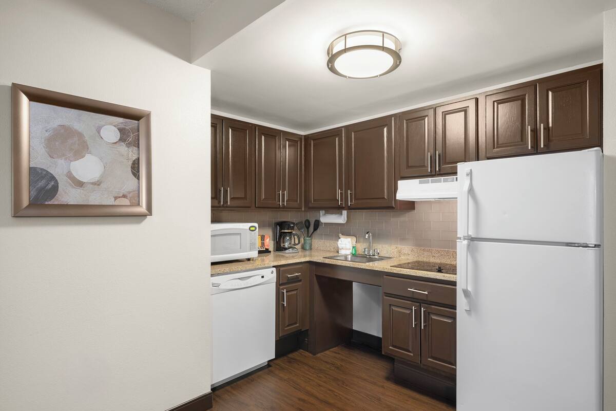 Una cocina compacta con armarios de madera, un refrigerador blanco, un microondas y una cafetera.