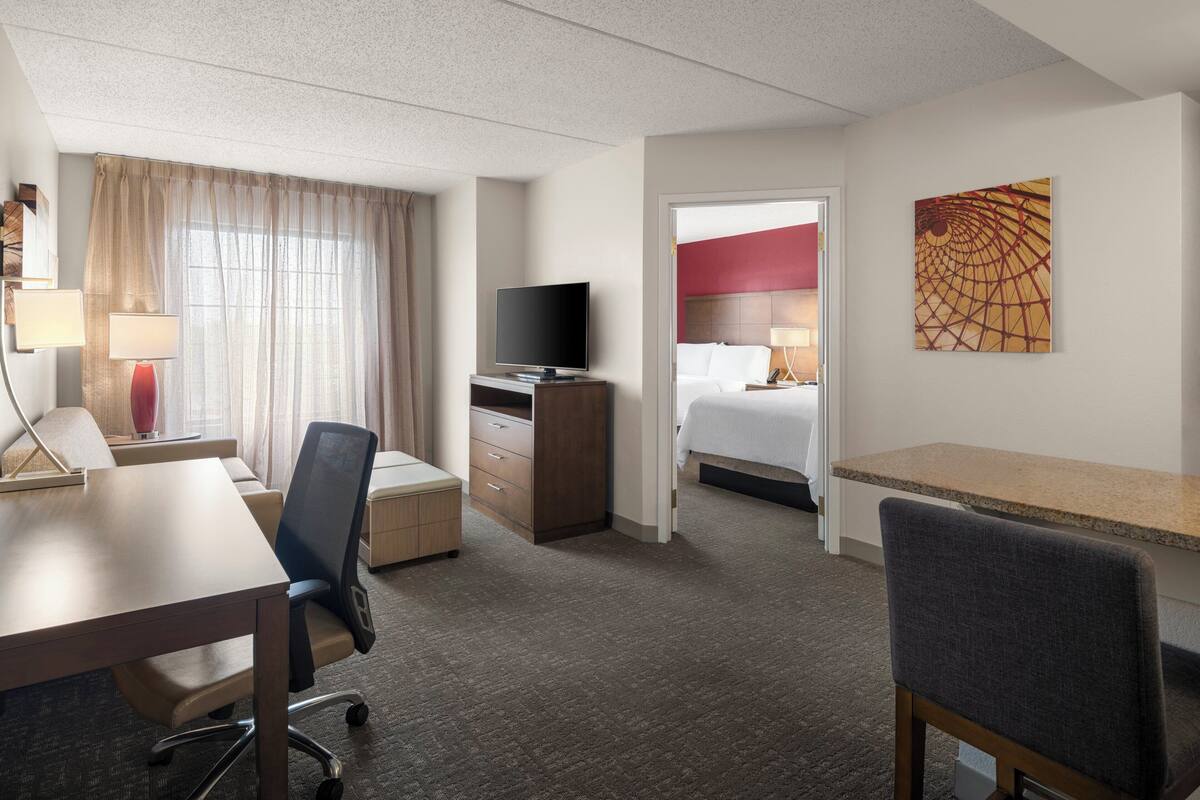 Una habitación de hotel con una cama, un escritorio, un televisor, una silla y un cuadro en la pared.