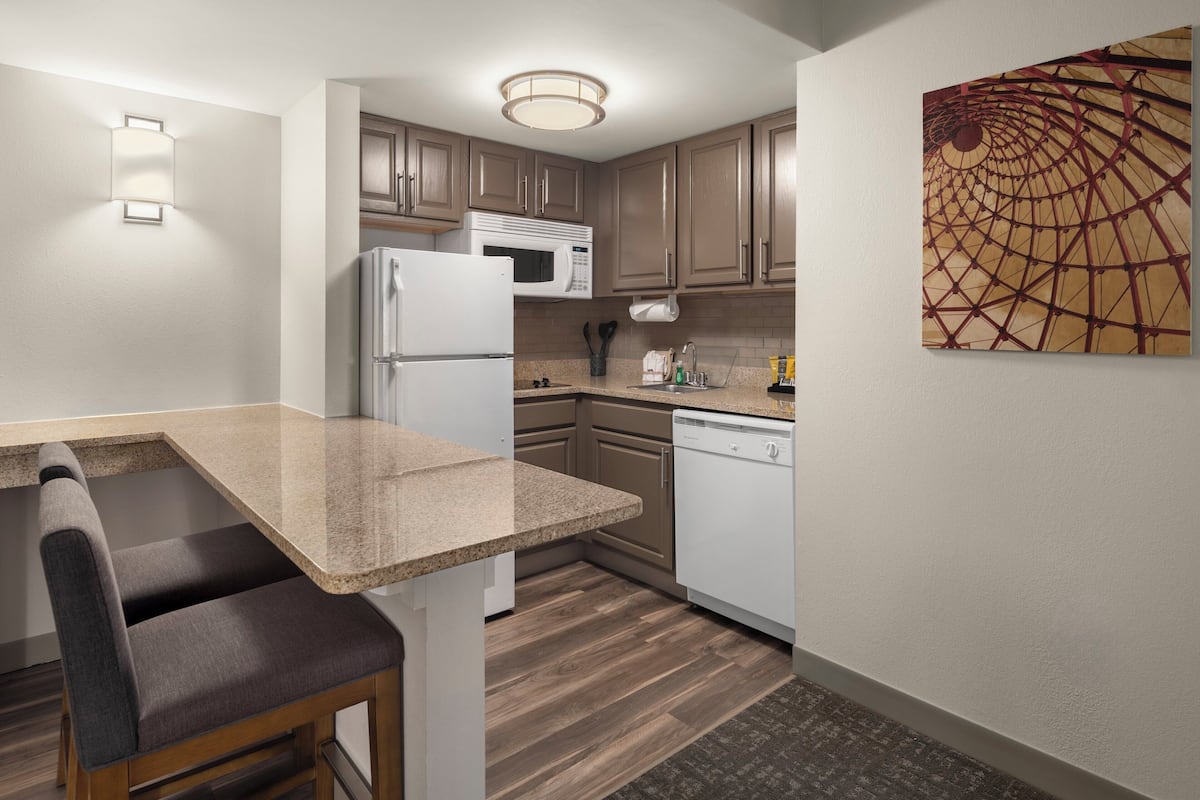 Cocina compacta con refrigerador, microondas y lavavajillas. Cuenta con una zona de comedor con un banco y una lámpara de pared.