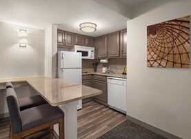 Cocina compacta con refrigerador, microondas y lavavajillas. Cuenta con una zona de comedor con un banco y una lámpara de pared.