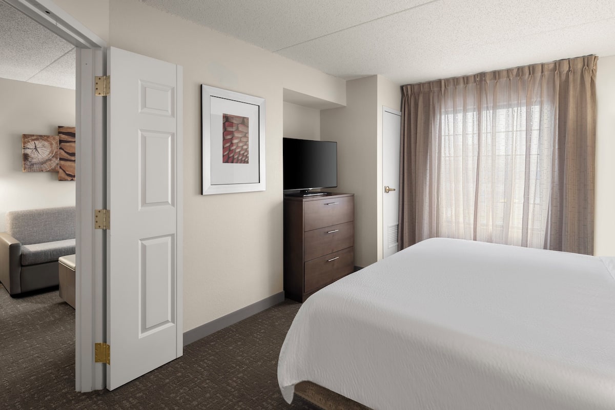 A hotel room with a bed, a TV on a dresser, a desk, and a chair.