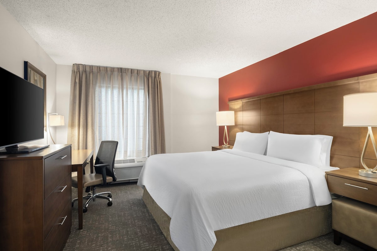 A hotel room with a large bed, a desk with a chair, a television, and a window with curtains.