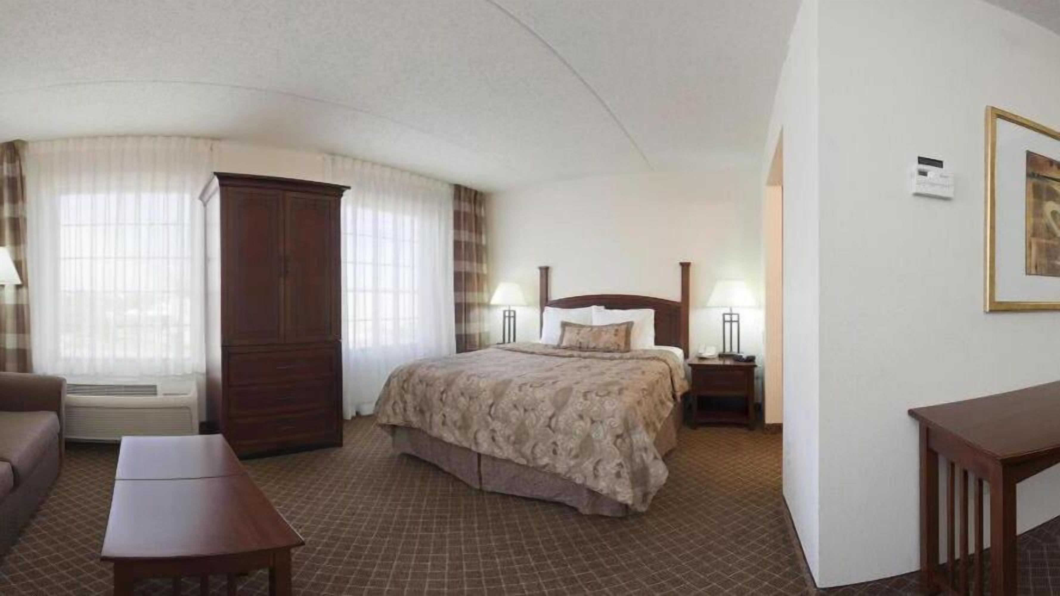 A hotel room with a bed, a desk, a chair, a wardrobe, and a window with curtains.