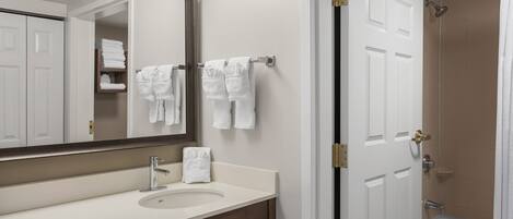 A bathroom with a sink, mirror, towel rack, and a shower area.