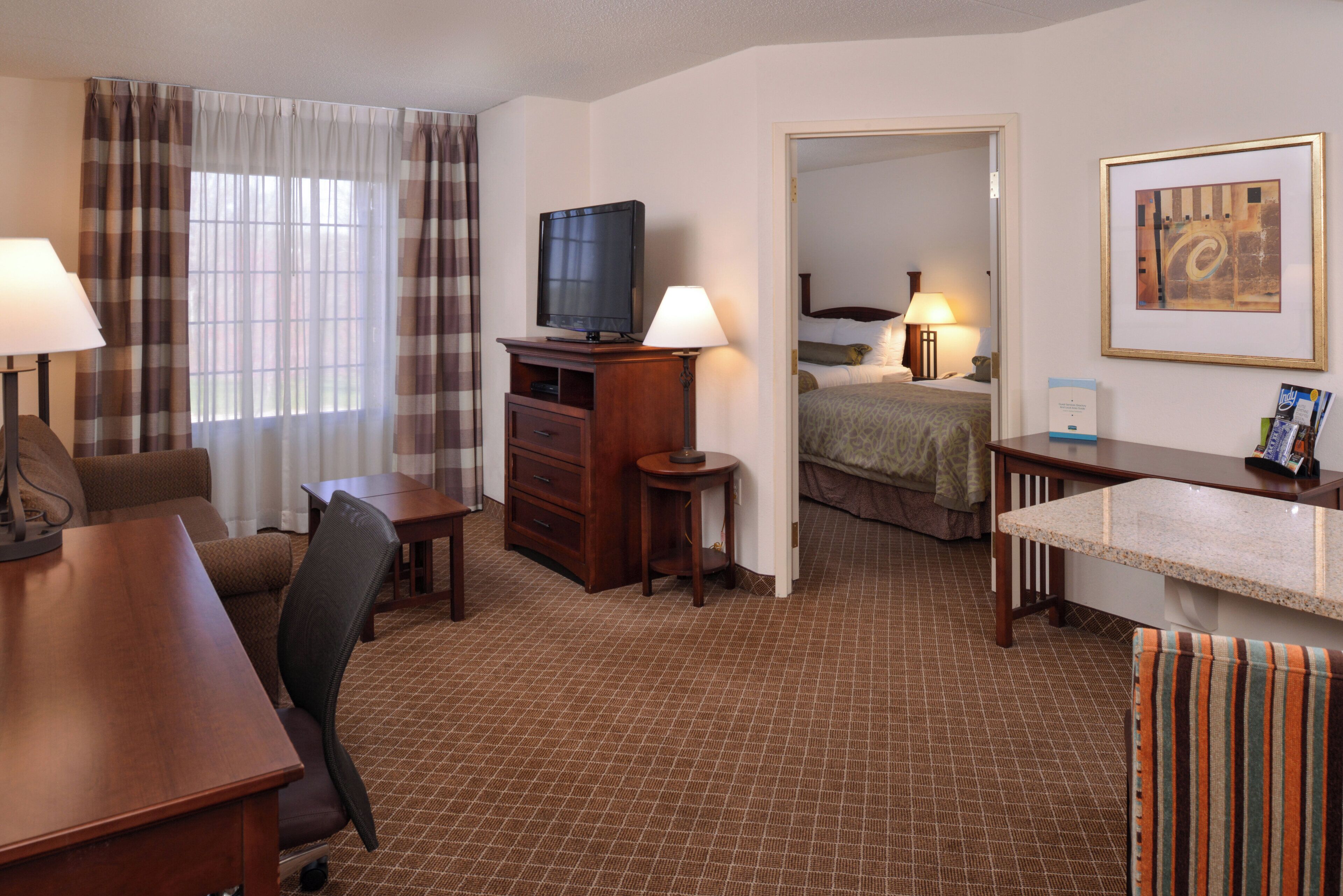 A hotel room with a desk, chair, television, and a bed.