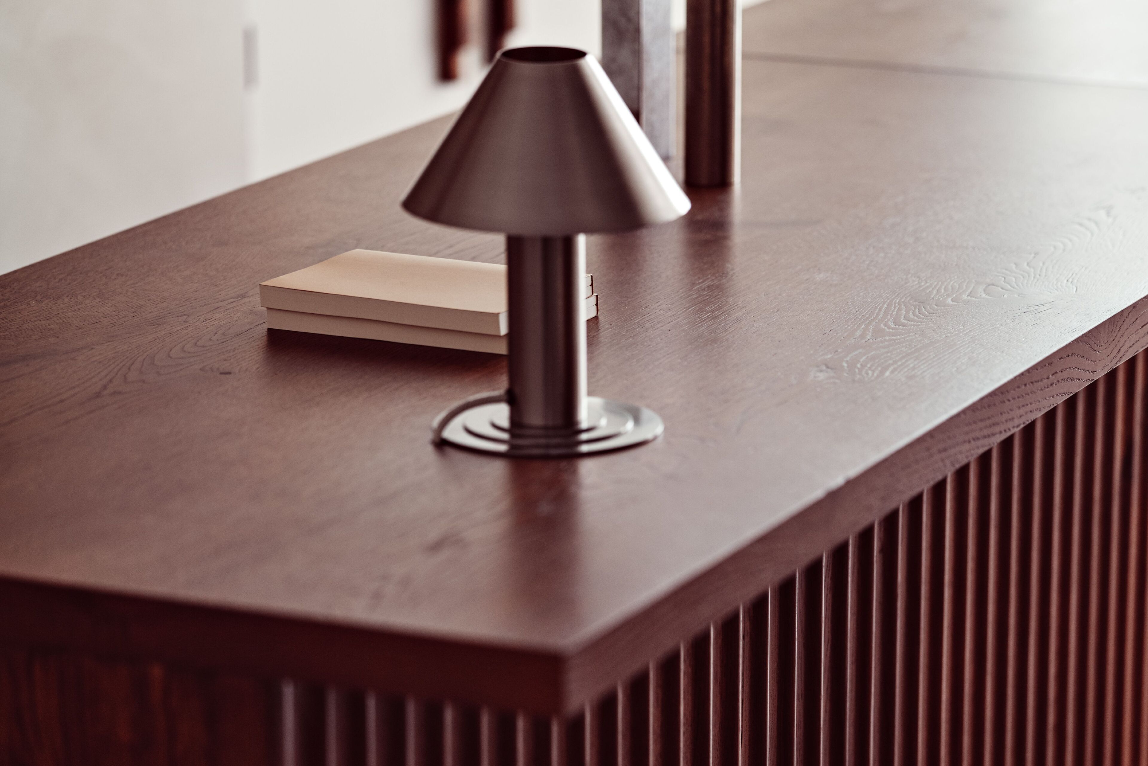 Een moderne lamp op een houten tafel, met een boek ernaast.