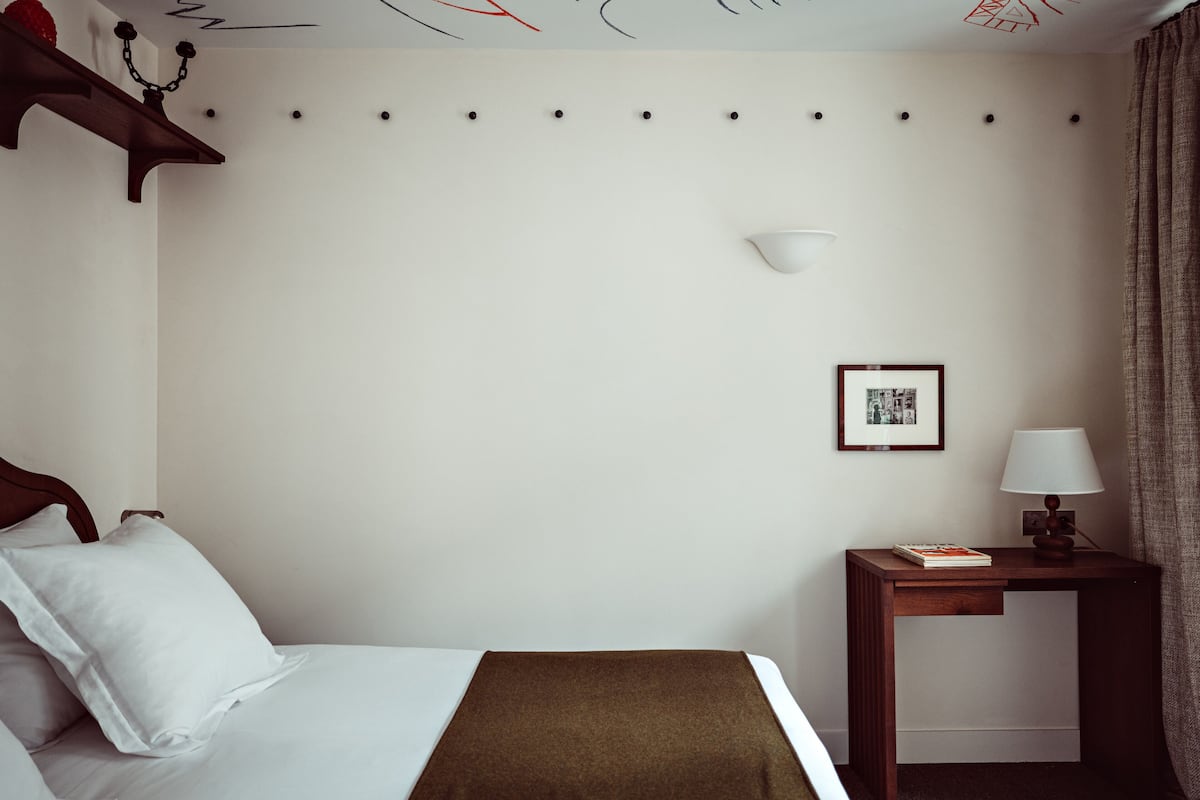 A hotel room with a bed, a bedside table with a lamp, a framed picture, and a wall-mounted shelf with a decorative item.