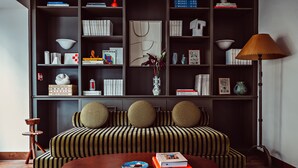 A modern living room with a striped sofa, a round coffee table, and a bookshelf filled with books and decorative items. - Hôtel des Académies et des Arts (Paris)
