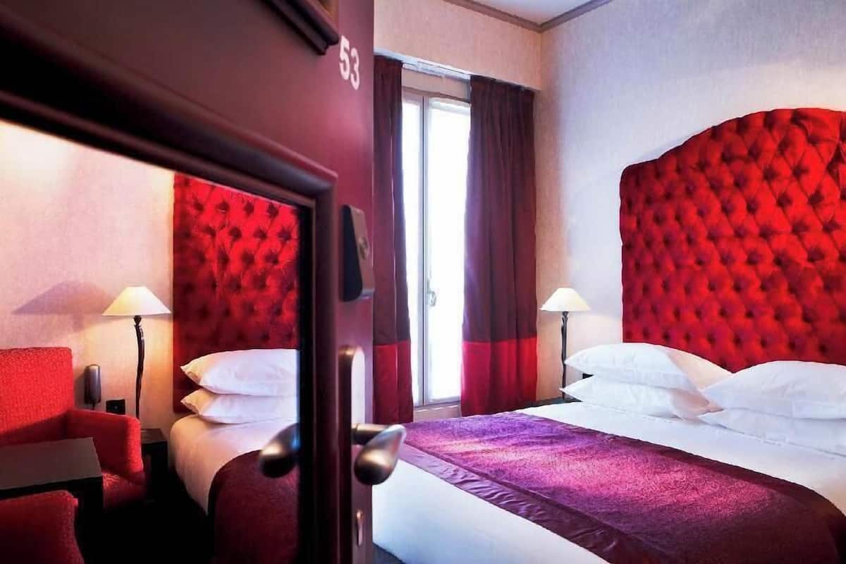 A hotel room with a large bed, two bedside tables, a red upholstered headboard, and a door with a number.