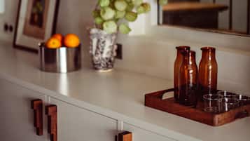 A kitchen counter with a metal container holding oranges, a decorative vase with green leaves, and two brown bottles on a wooden tray.