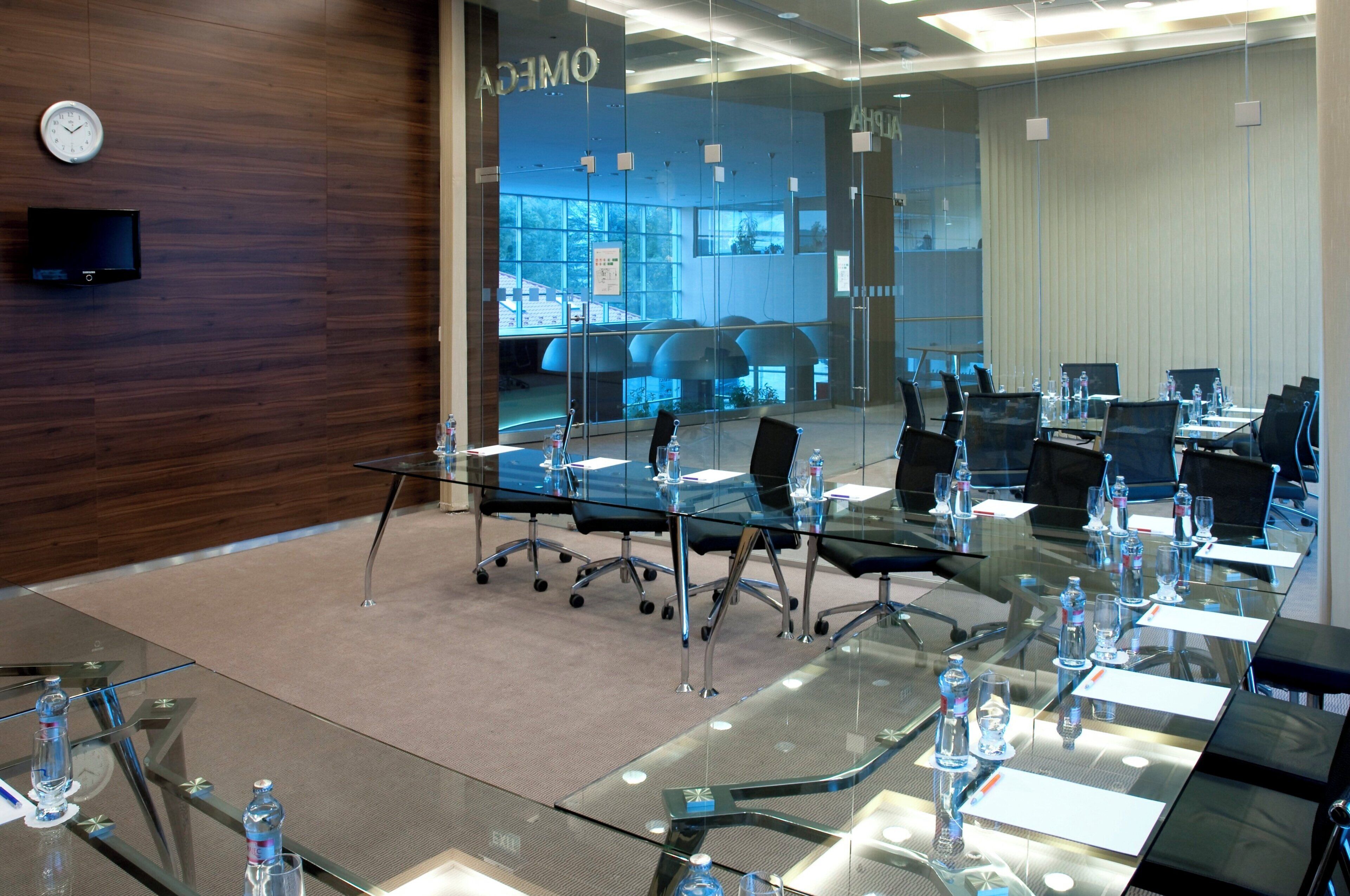 A modern conference room with glass tables, black chairs, and a clock on the wall.