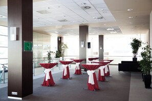A conference room with multiple tables, a large plant, and a sign indicating room directions.