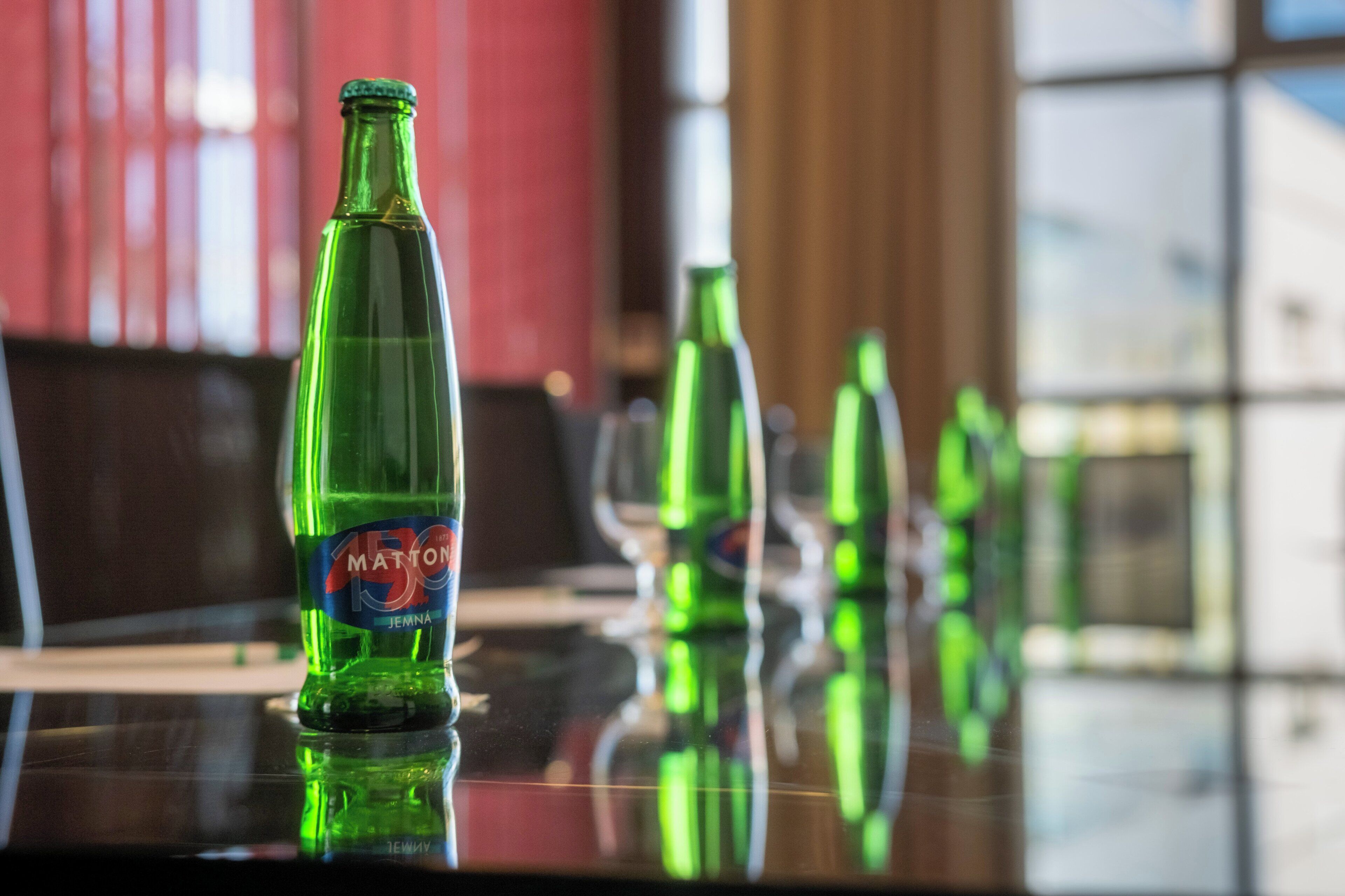 A glass table with a green bottle labeled "Matton" and reflections of other green bottles.