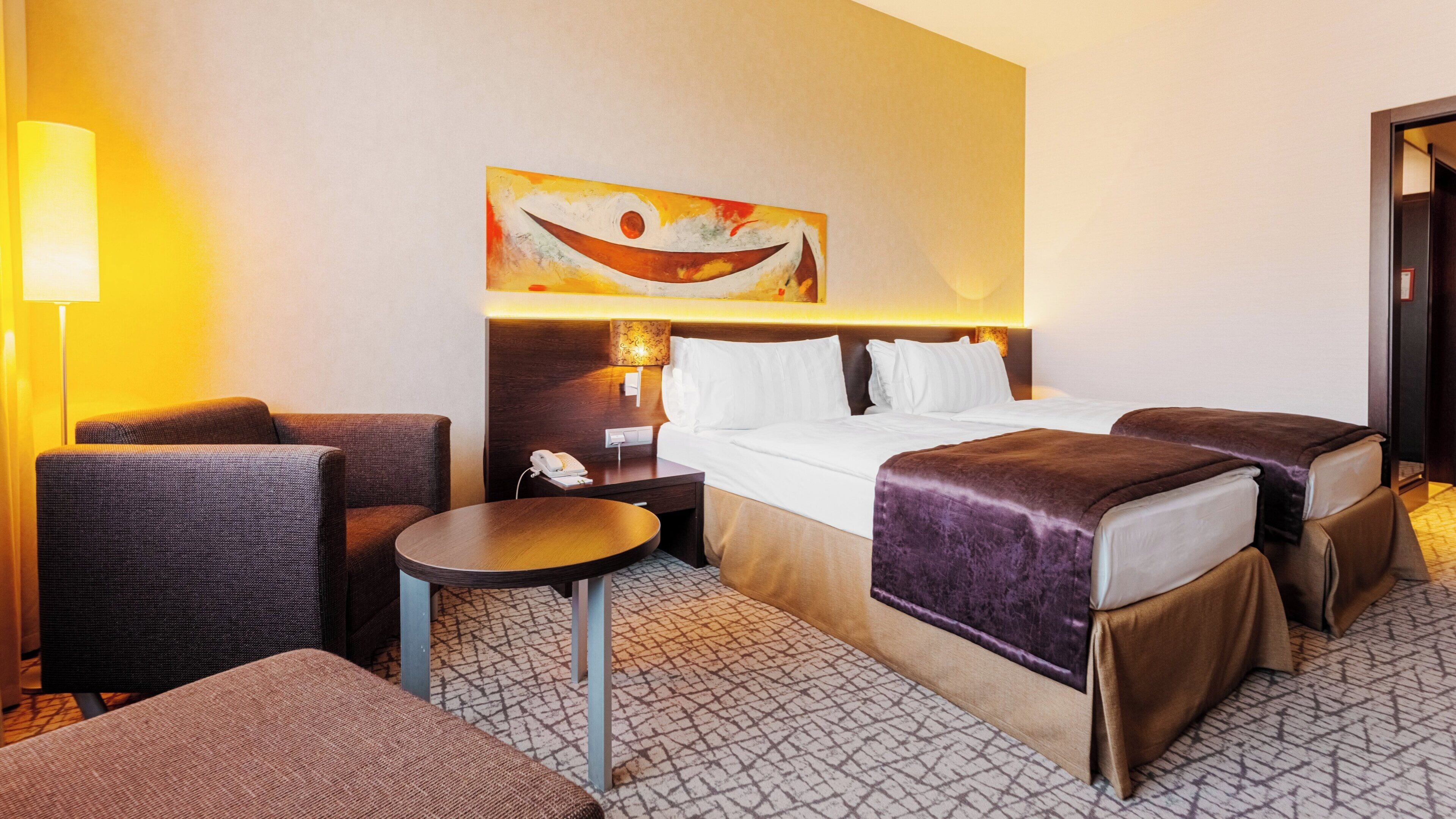 A hotel room with a bed, two bedside tables, a chair, and a lamp.