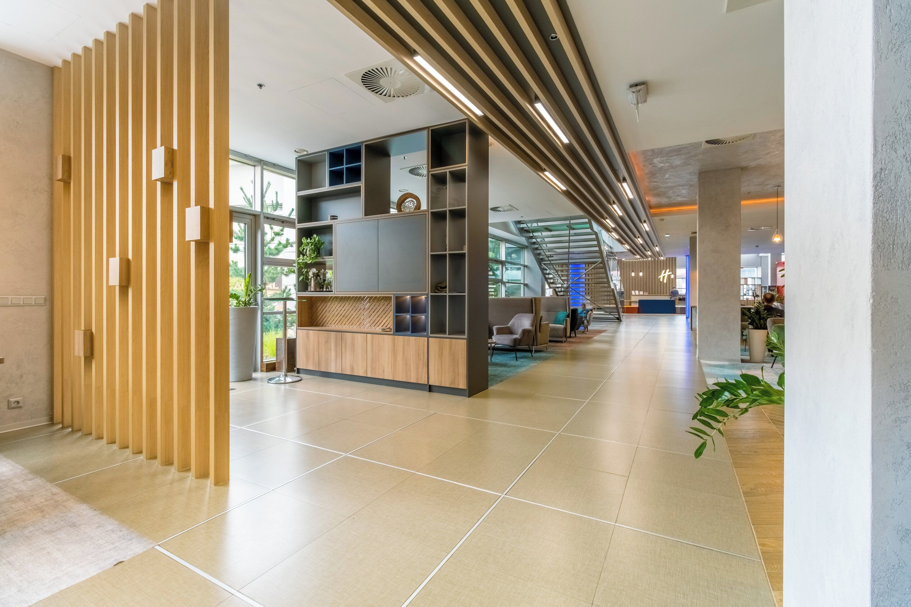 Un moderno vestíbulo de hotel con mostrador de recepción, zona de estar y una escalera que conduce a pisos superiores.