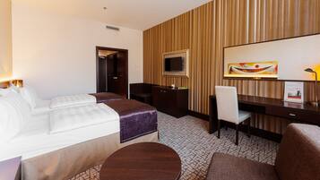 A hotel room with a bed, a desk, a chair, a TV, and a painting on the wall.