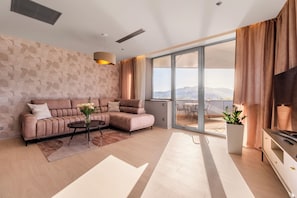 Ein modernes Wohnzimmer mit einem Ecksofa, einem Couchtisch und einem großen Fenster mit Blick ins Freie.