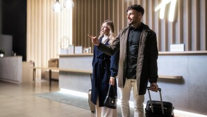 Een moderne hotel lobby met een receptiebalie, hangende verlichting en een groot verlicht bord.