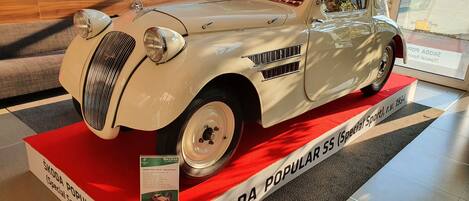 Un coche clásico ŠKODA POPULAR SS expuesto sobre una alfombra roja y un cartel informativo.
