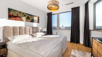 Ett modernt hotellrum med en stor säng, ett skrivbord och utsikt över staden genom stora fönster.