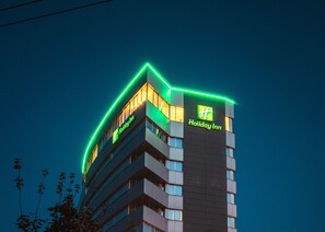 A Holiday Inn hotel building with a modern design, featuring multiple floors and a prominent green neon sign.