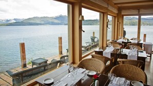 A restaurant with tables set for dining, overlooking a lake with mountains in the background. - Correntoso Lake & River Hotel (Villa La Angostura)