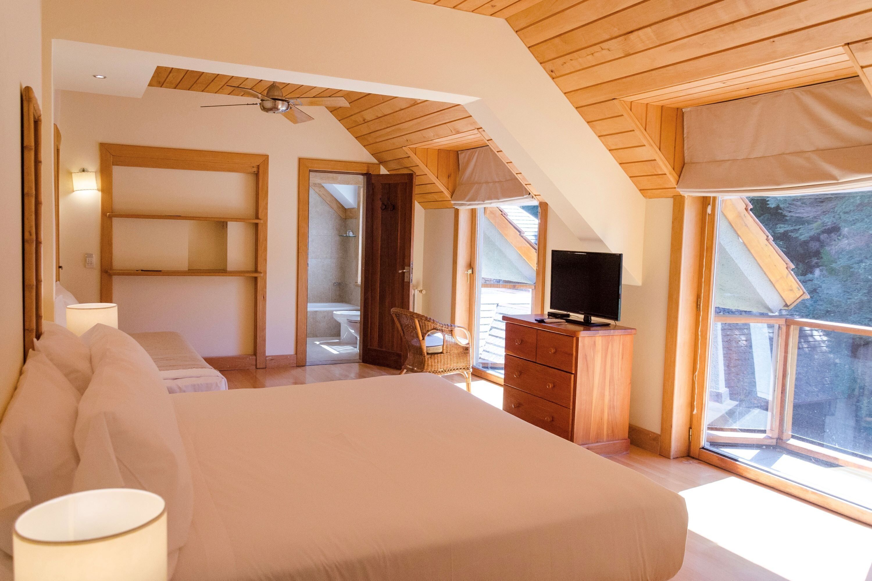 Ein Schlafzimmer mit einem großen Bett, Holzboden, einem Fernseher und einem Fenster mit Blick ins Freie.