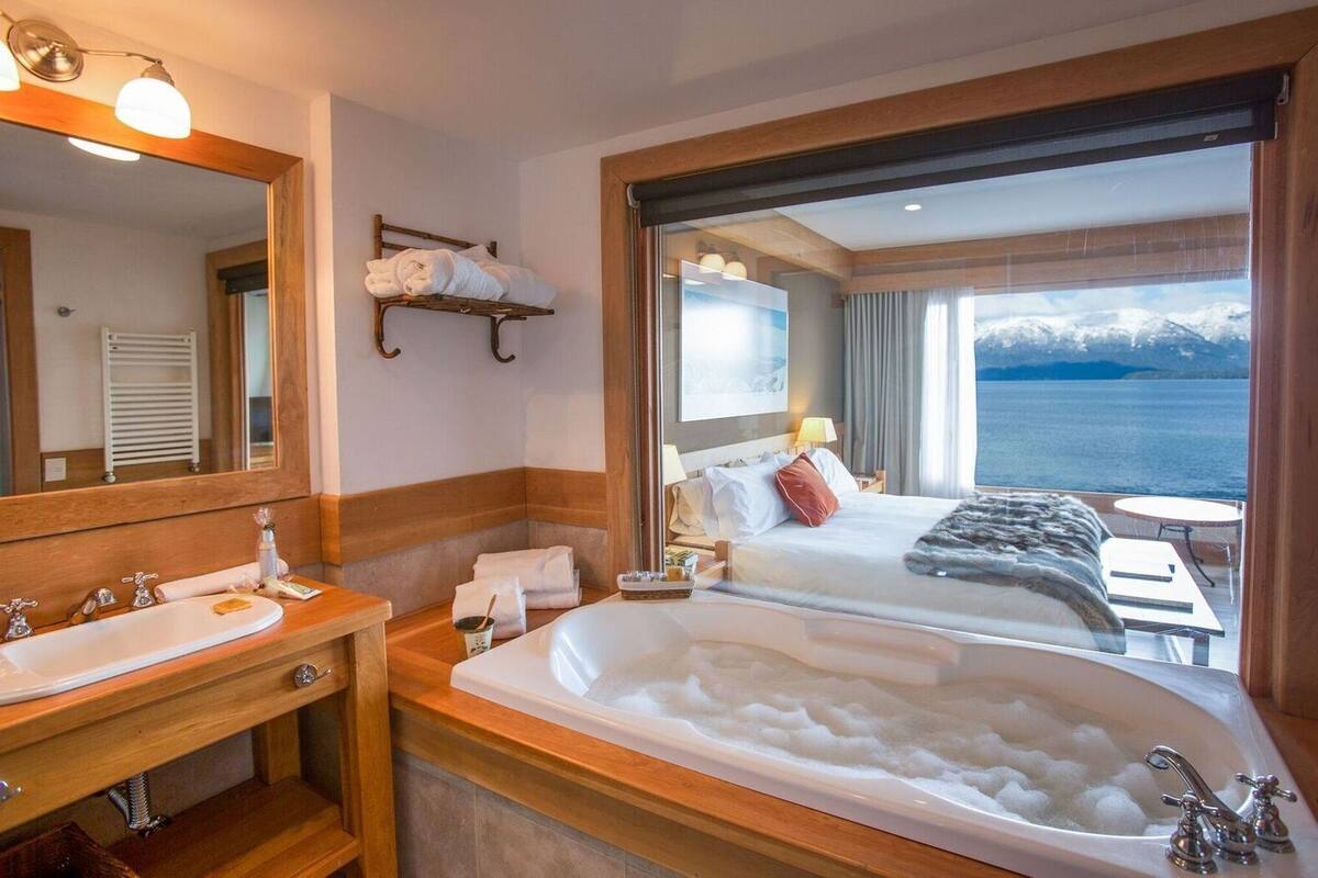 Ett hotellrum med ett stort badkar, en dubbelsäng, en sittgrupp med utsikt över havet och ett badrum med handfat och spegel.
