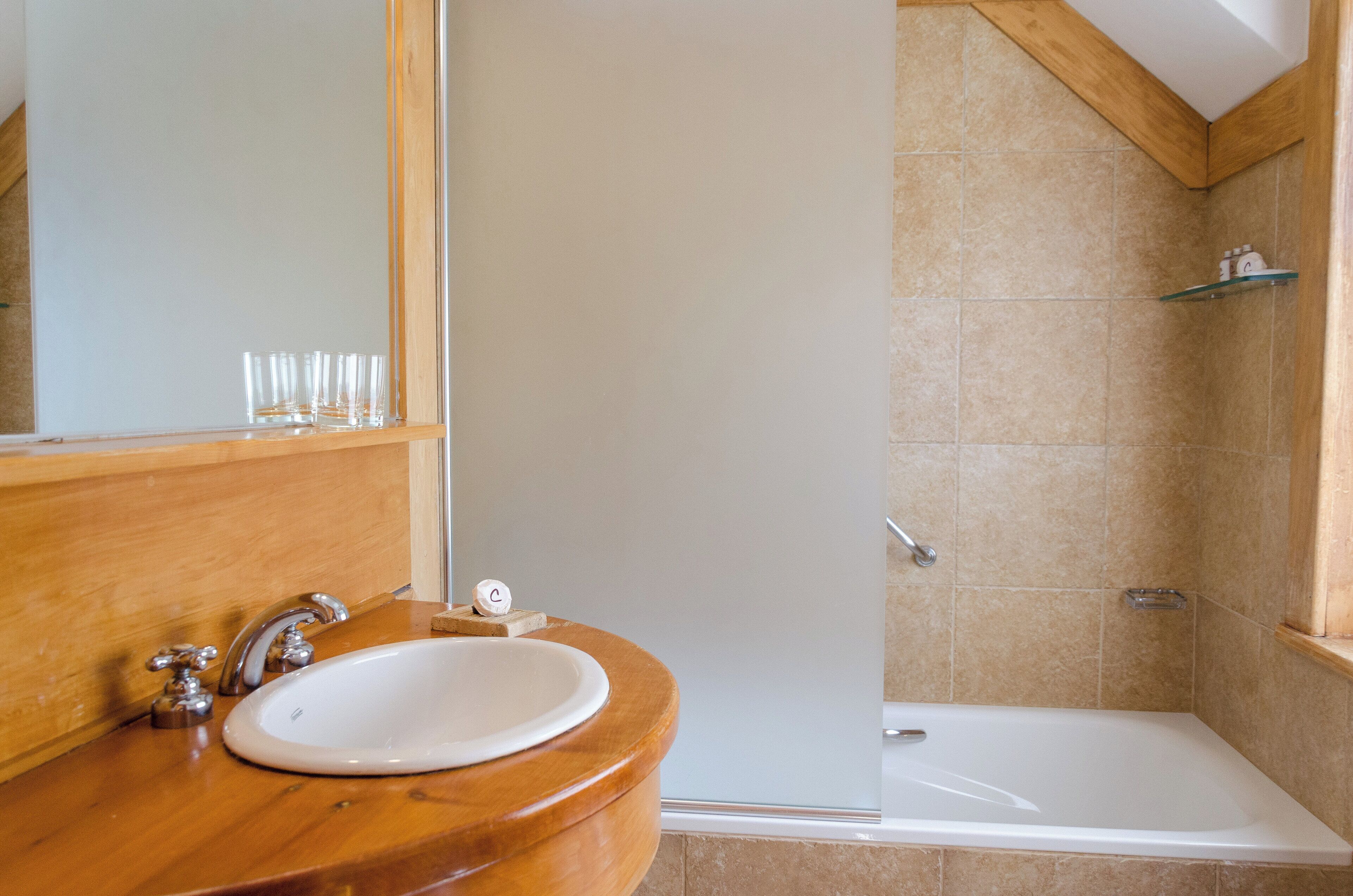 A bathroom with a wooden vanity, a white sink, a mirror, and a shower area.