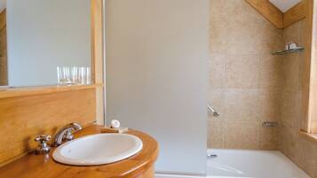 A bathroom with a wooden vanity, a white sink, a mirror, and a shower area.