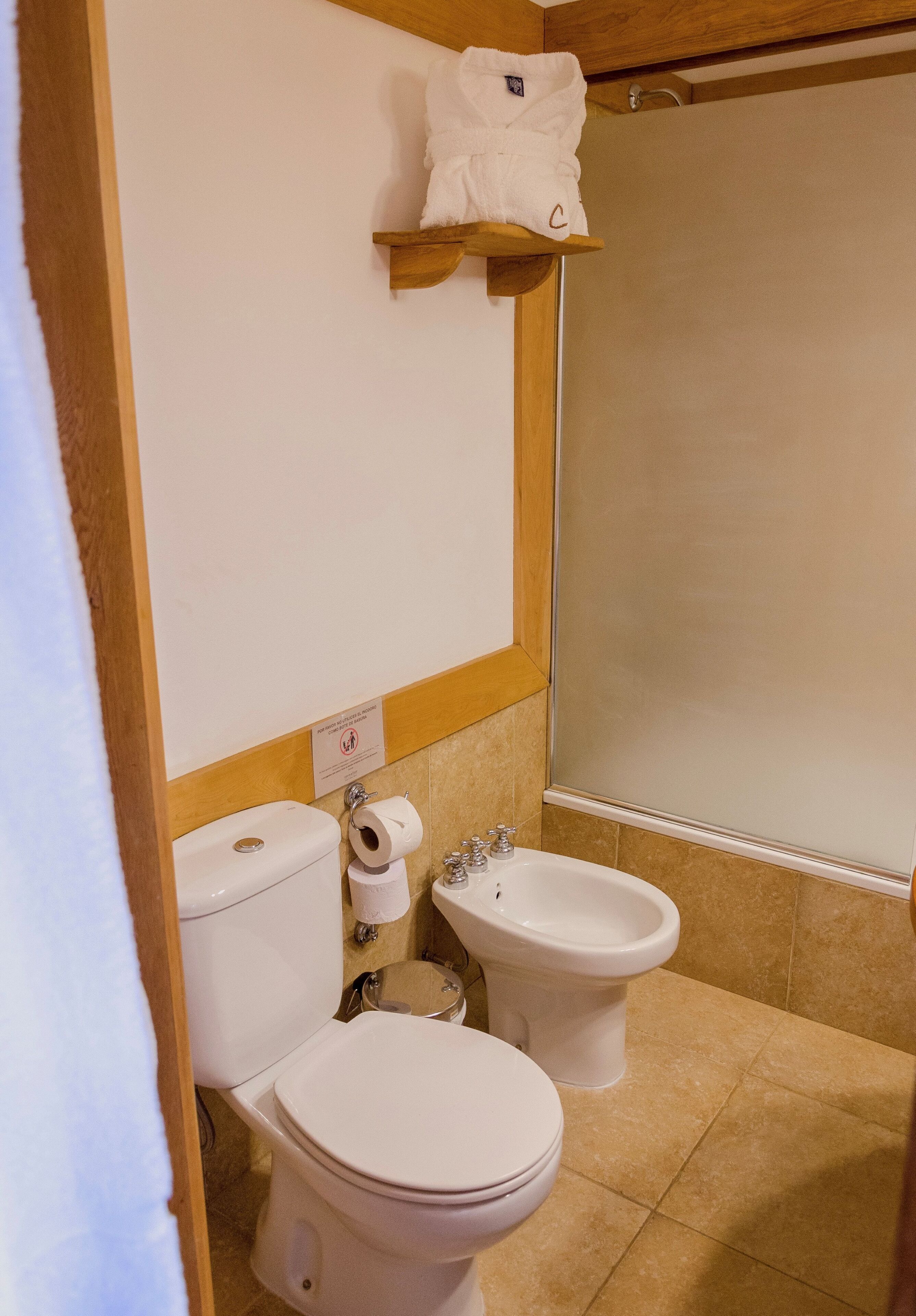 Une salle de bain équipée de toilettes, d’un bidet et d’une étagère sur laquelle est posée une serviette.