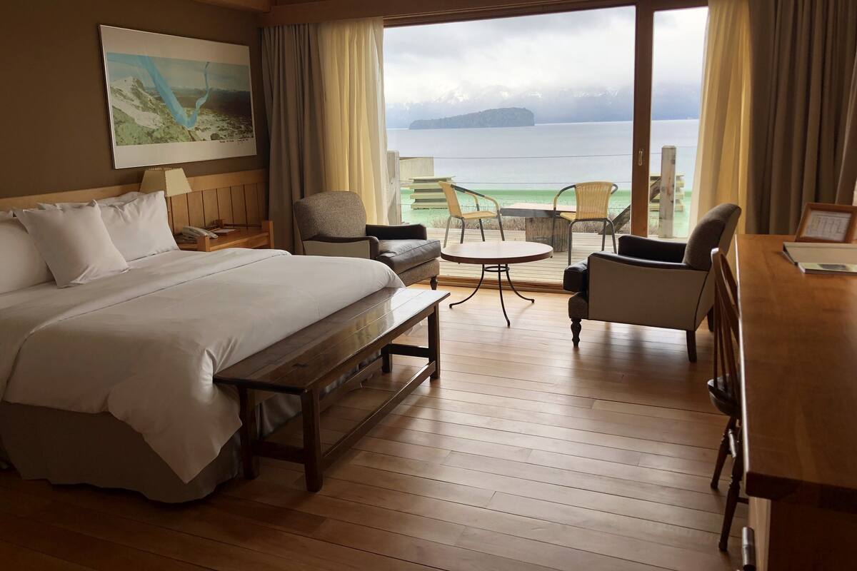 Ett hotellrum med en säng, ett skrivbord, två stolar, ett litet bord och utsikt över havet.