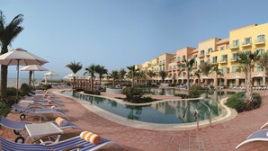 Ein Poolbereich eines Resorts mit Liegestühlen und Sonnenschirmen, einem Pool und einem Gebäude mit Balkonen.