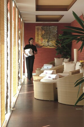 Un vestíbulo de hotel con sofás de mimbre, una planta grande y una persona cargando toallas.
