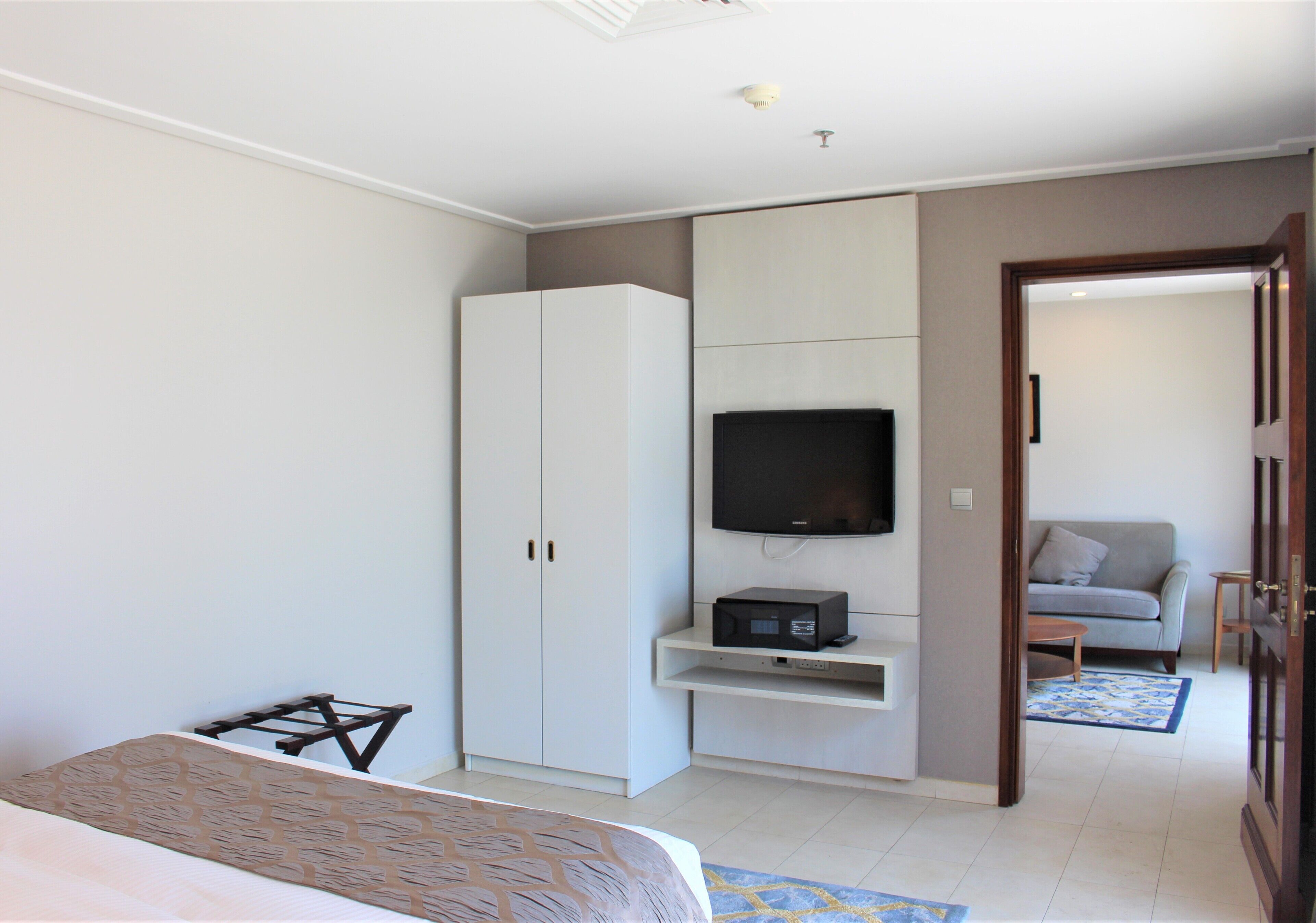 A bedroom with a bed, a wardrobe, a TV, and a small table.