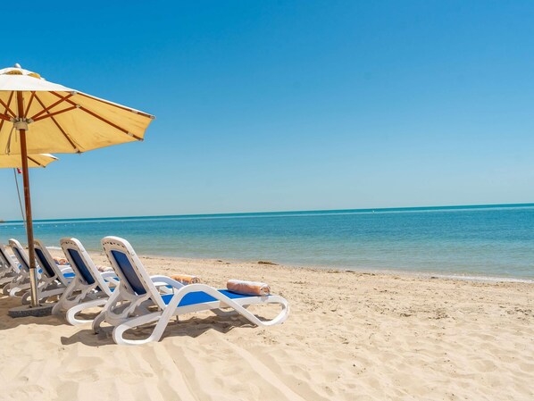 A beach with sun loungers and a yellow umbrella.