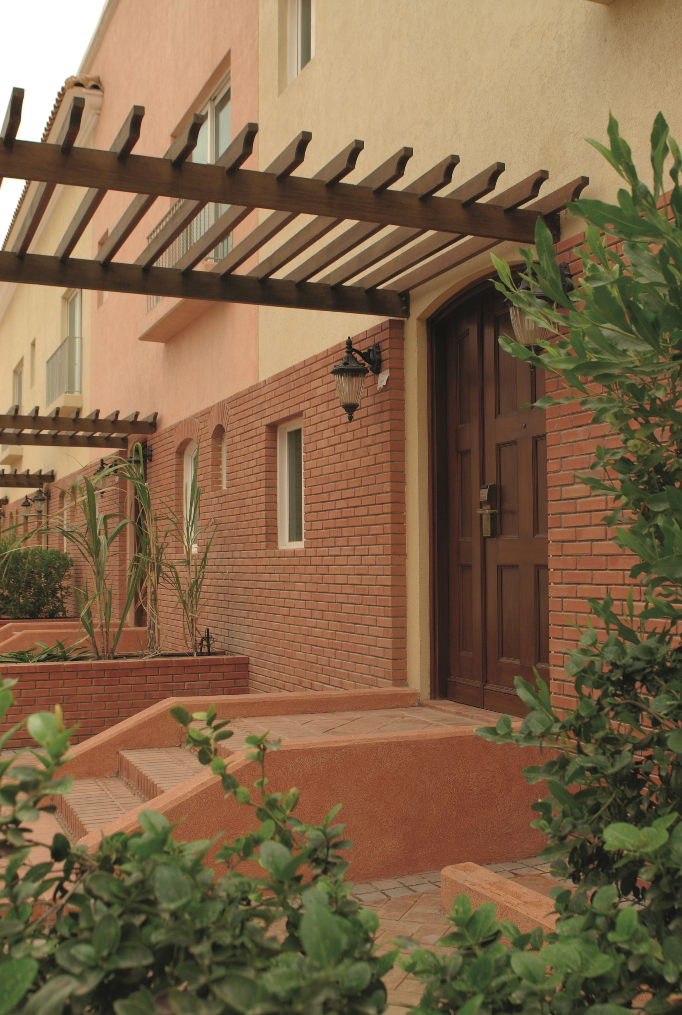 Un edificio con fachada de ladrillo, una pérgola de madera y una puerta con ventanal.