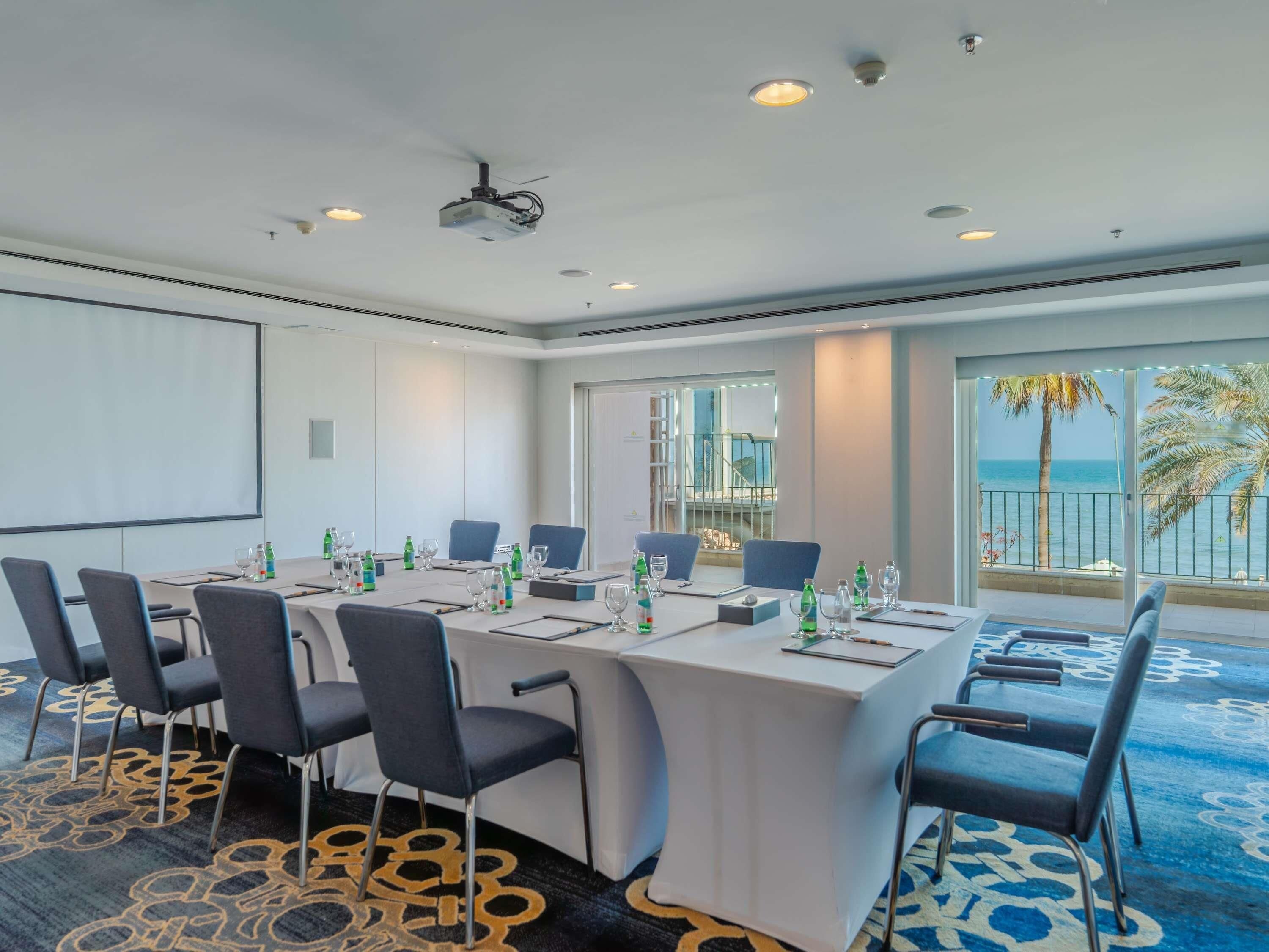 A conference room with a large table, chairs, a projector, and a view of the ocean.