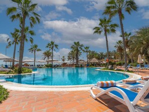 A pool area with lounge chairs, palm trees, and umbrellas.